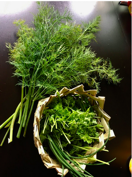 A bunch of dill next to a basket of greens