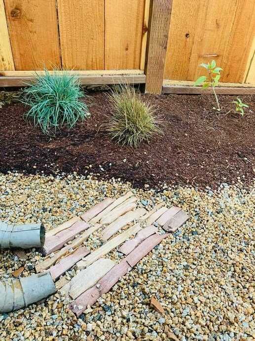 A wooden fence is surrounded by gravel and bricks.