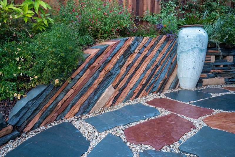 A white vase is sitting on a stone patio next to a wooden wall.