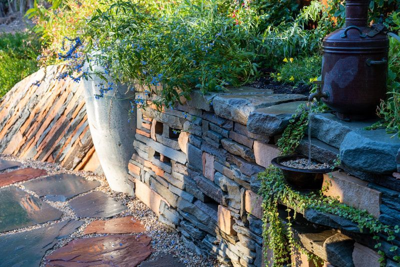 A stone wall with potted plants and a fountain in a garden.
