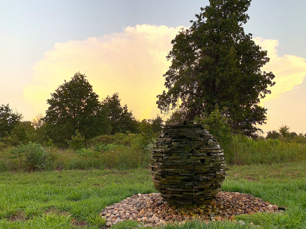 A sculpture in the middle of a grassy field with trees in the background.