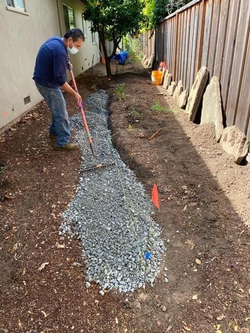 A man wearing a mask is raking gravel in a yard.