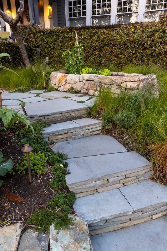 A stone walkway leading to a house in a garden.