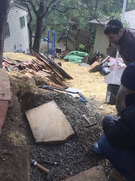 A man is kneeling down in front of a pile of wood.