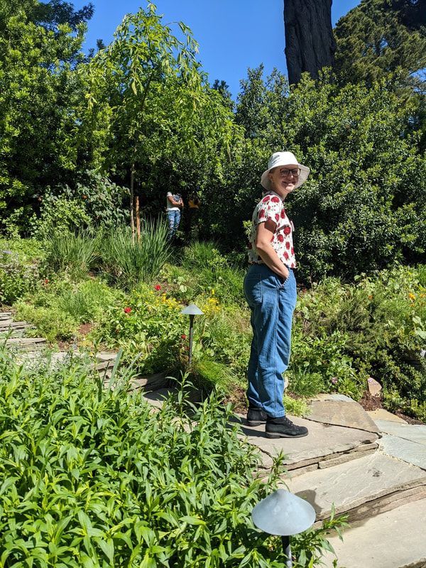 A woman in a hat is standing on a set of steps in a garden.