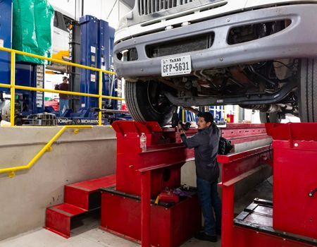 Mechanic working under a truck raised on a red lift in a repair shop.