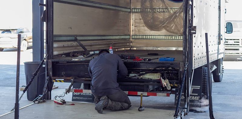 A person kneels, working on the back of a truck. Tools and parts are scattered around.