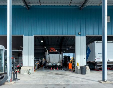 Tree trimming service in progress; a cherry picker lifts a worker to cut branches. A skid steer, logs