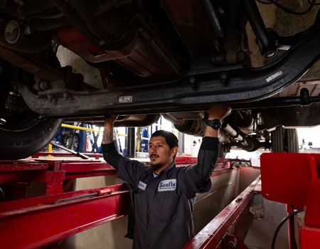 Mechanic working under a car on a lift in a garage, raising his arms.