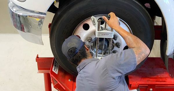 Mechanic aligns truck tire with a measurement tool.