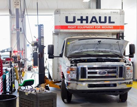 U-Haul truck on a lift with hood open in a repair shop.