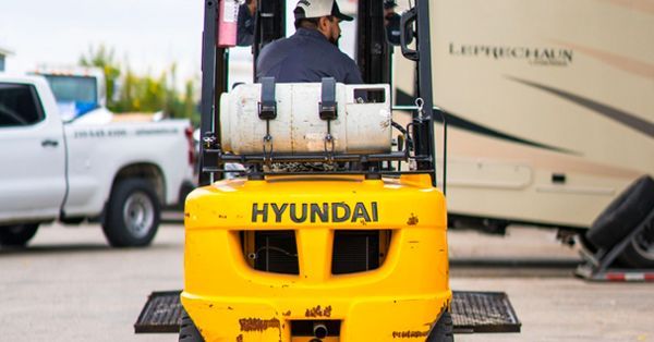 Yellow Hyundai forklift with driver, parked in front of a camper.