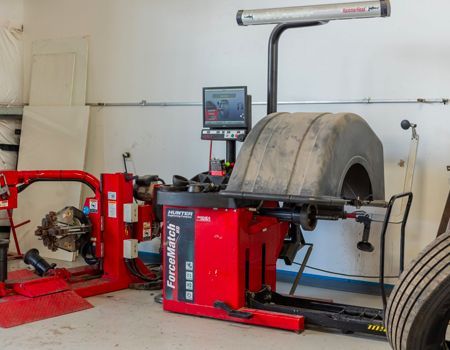 A tire balancing machine in a garage, red and black, with a tire mounted on it.