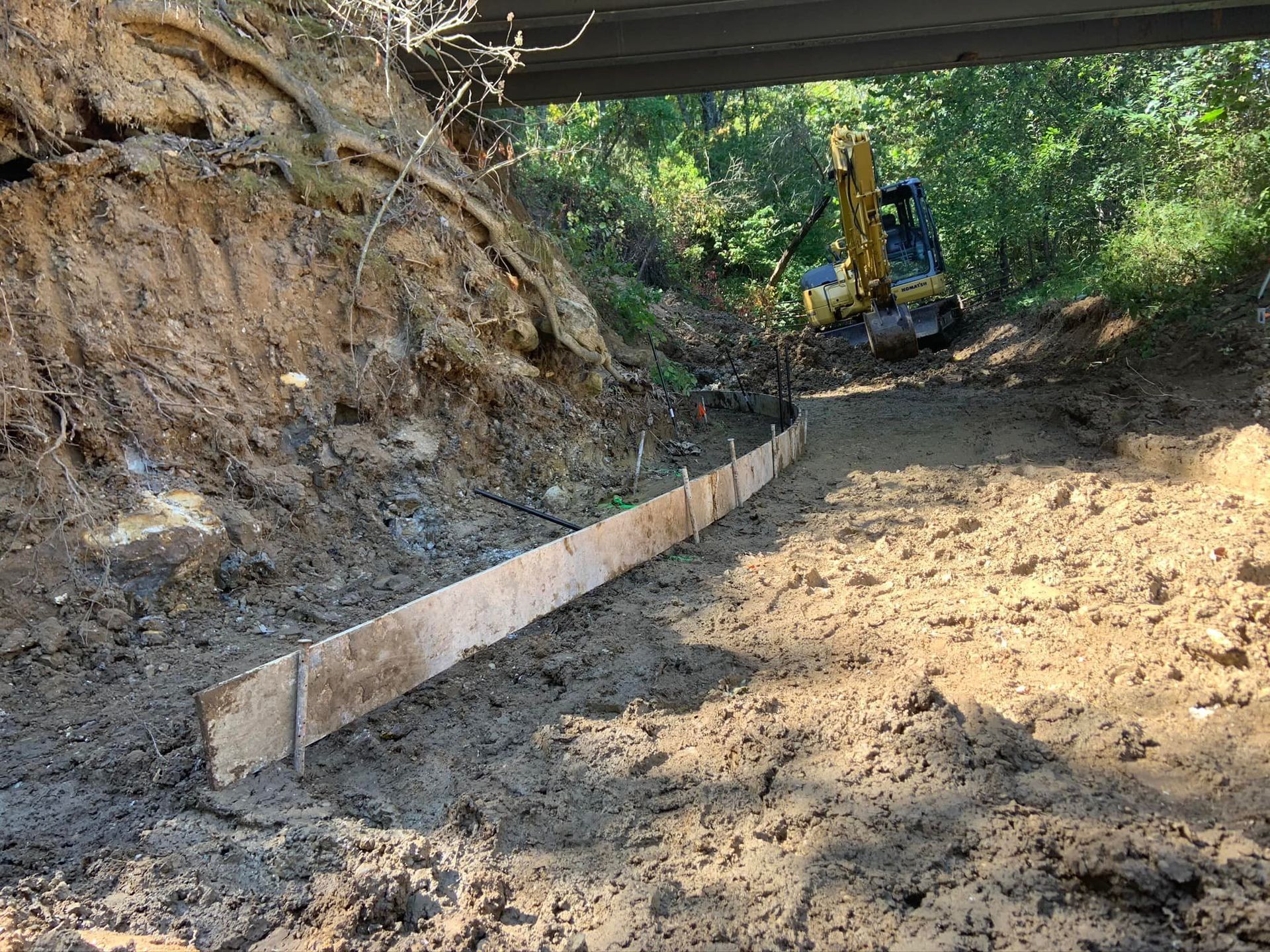 Construction site under bridge with wooden formwork and excavator.