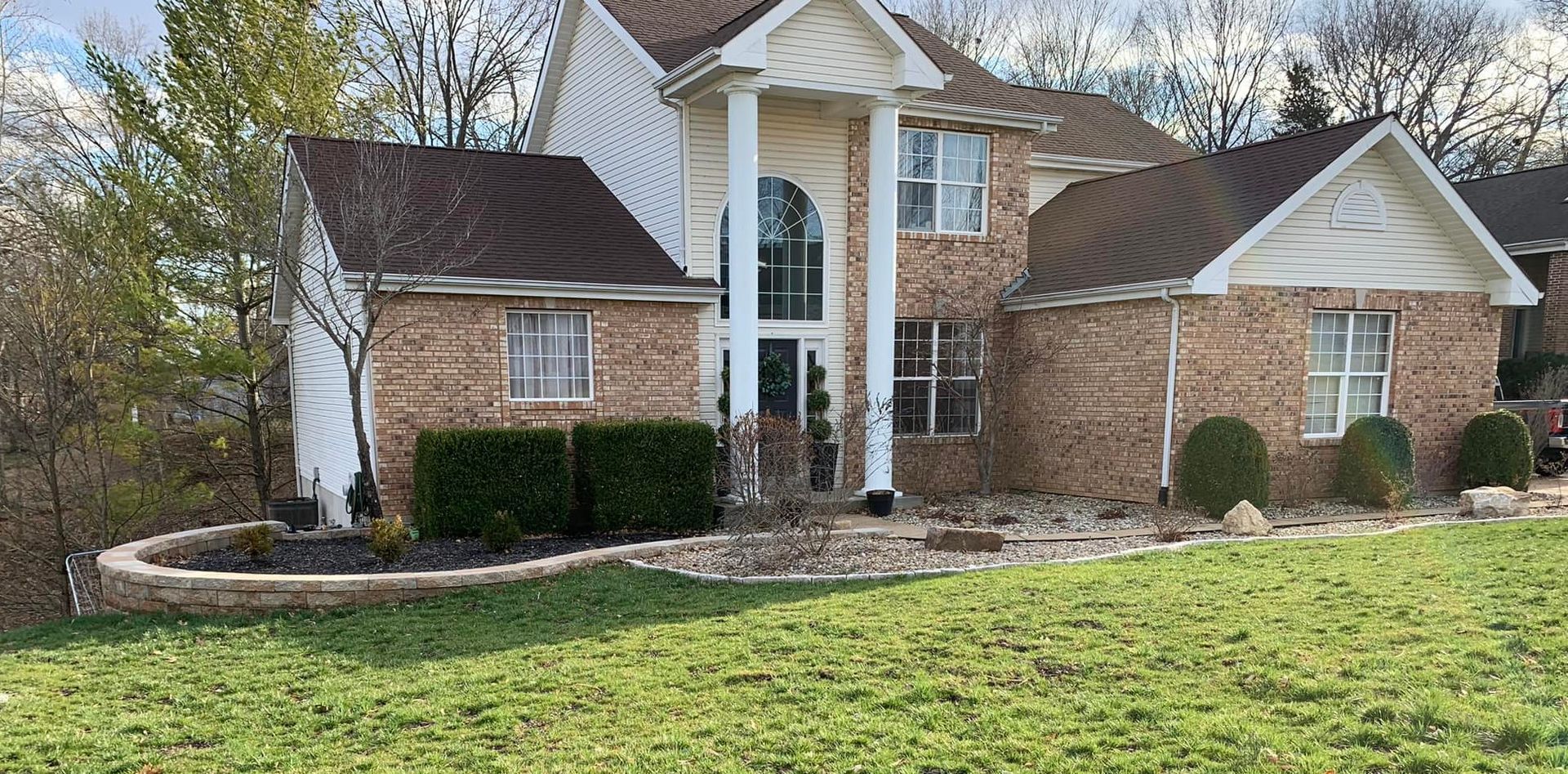 Brick house with columns, manicured lawn, and landscaping.