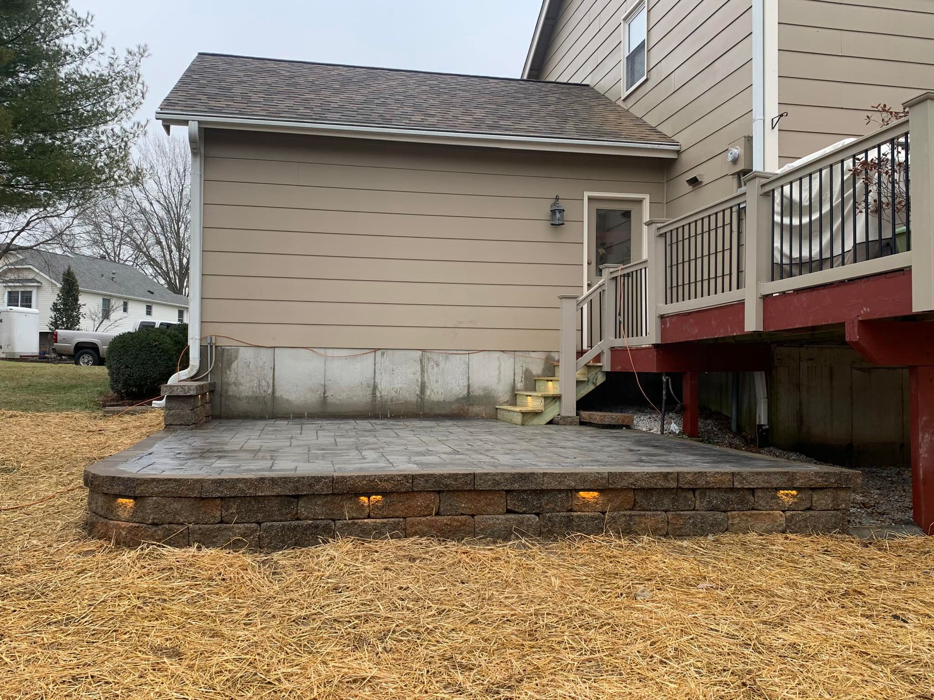 Stone patio with low brick retaining wall, next to a house with a deck.
