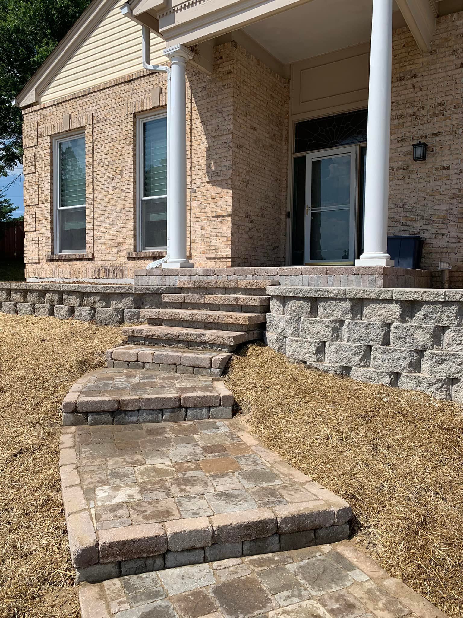 Brick home entrance with stone steps and retaining walls, surrounded by gravel.