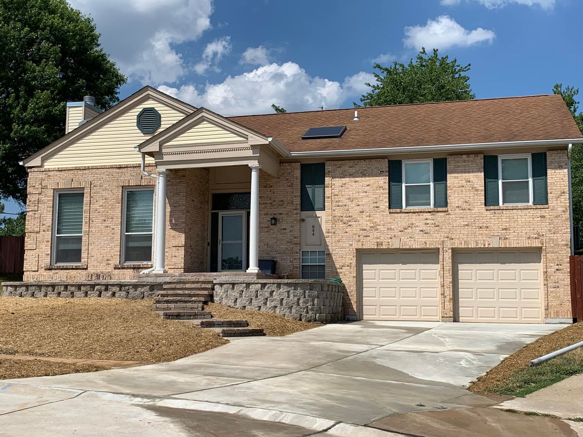 Two-story brick house with beige garage doors, front porch, and driveway on a sunny day.