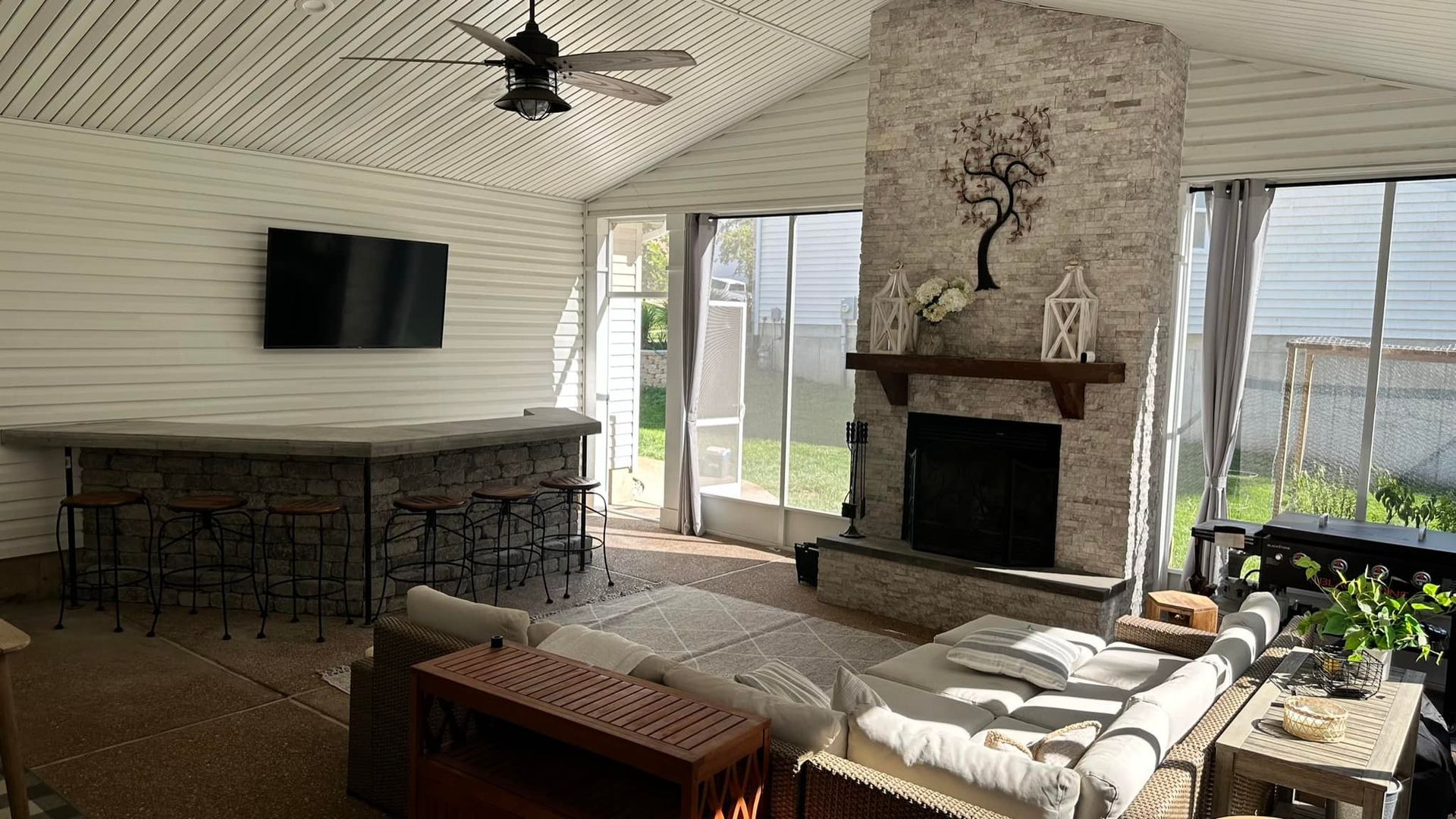 Sunroom with bar, fireplace, and seating; neutral tones; TV mounted; ceiling fan.