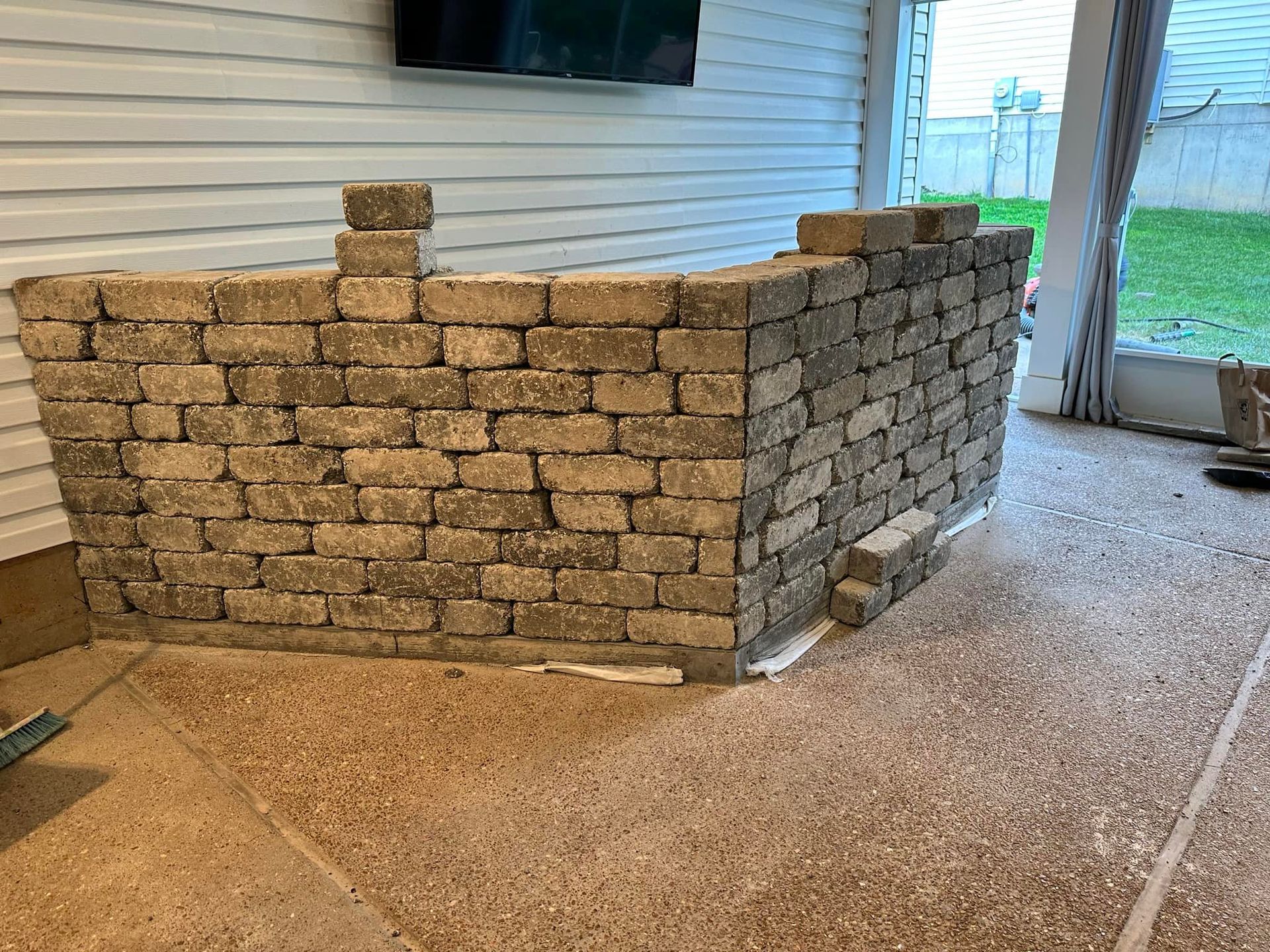 Brick wall construction on a patio, with gray bricks, a television, and a glass door.