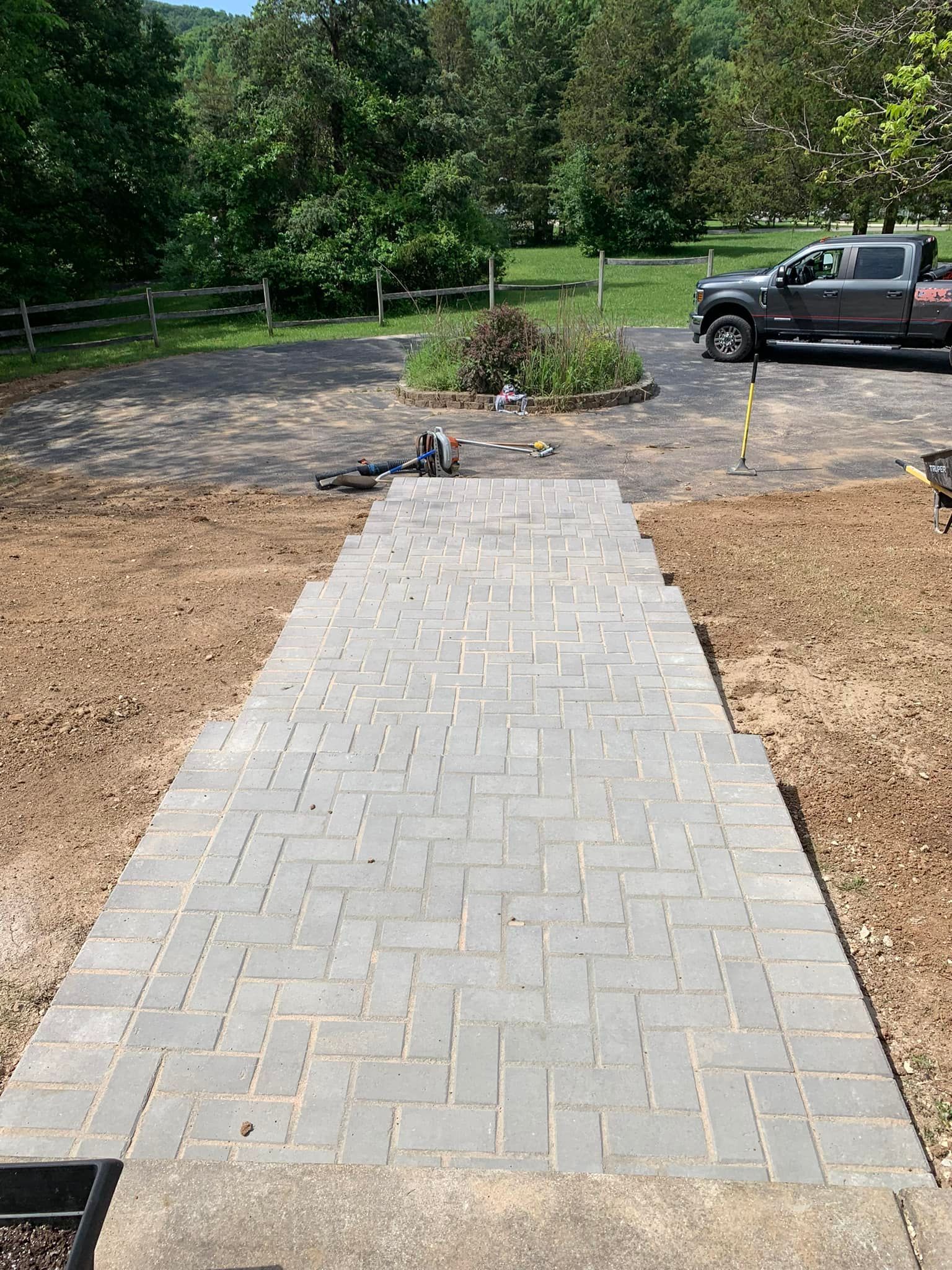 Grey brick pathway leading from a concrete surface to a small garden bed and a driveway.