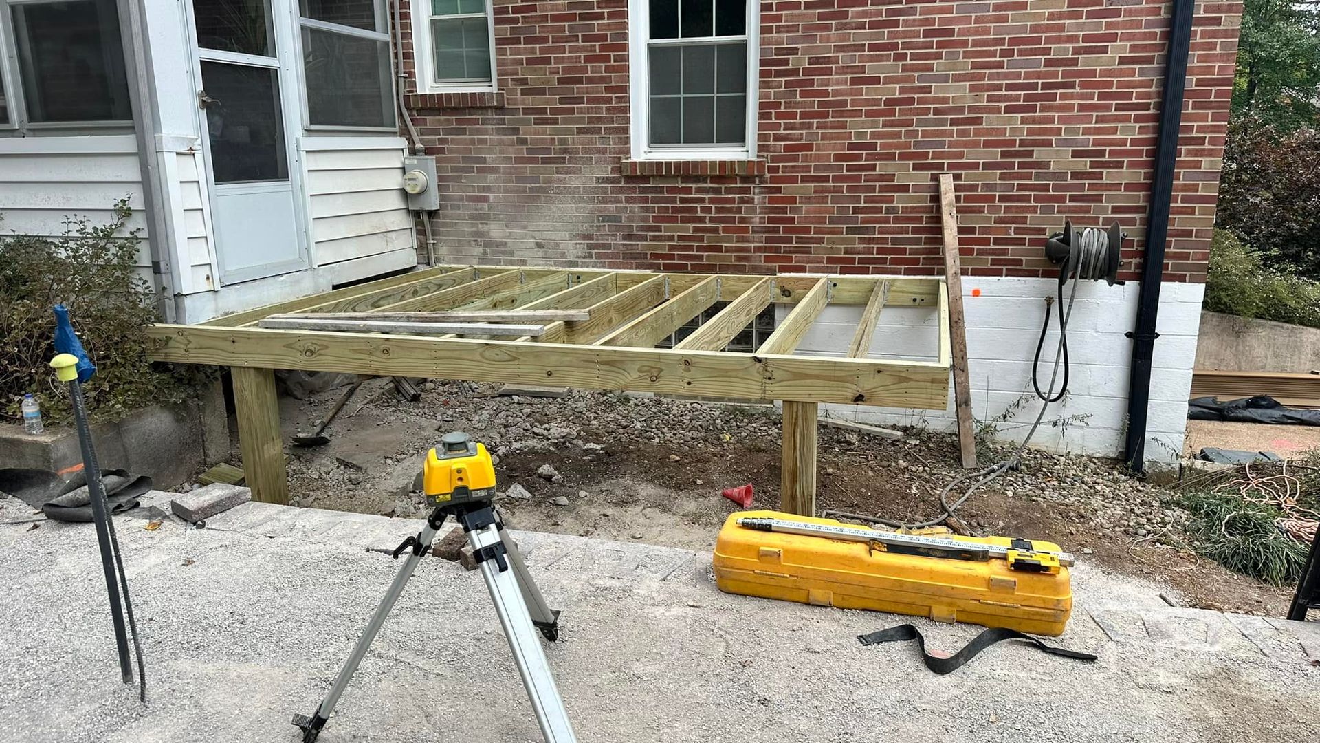 Deck frame construction against a brick building; a laser level and tools are present.