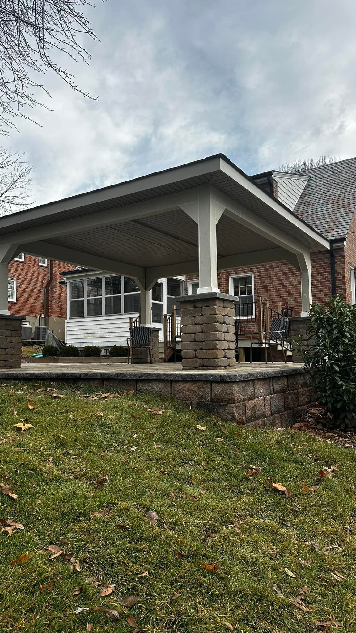 Covered patio with brick columns, seating, and view of a house. Overcast sky.