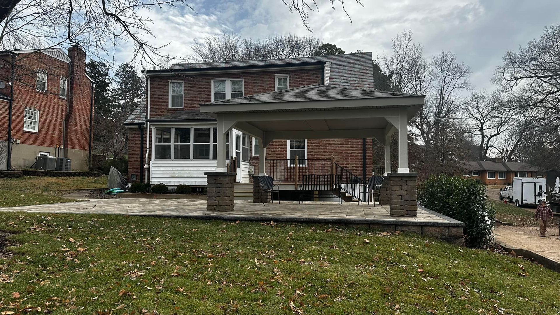Brick house with a covered patio in a yard, under an overcast sky.