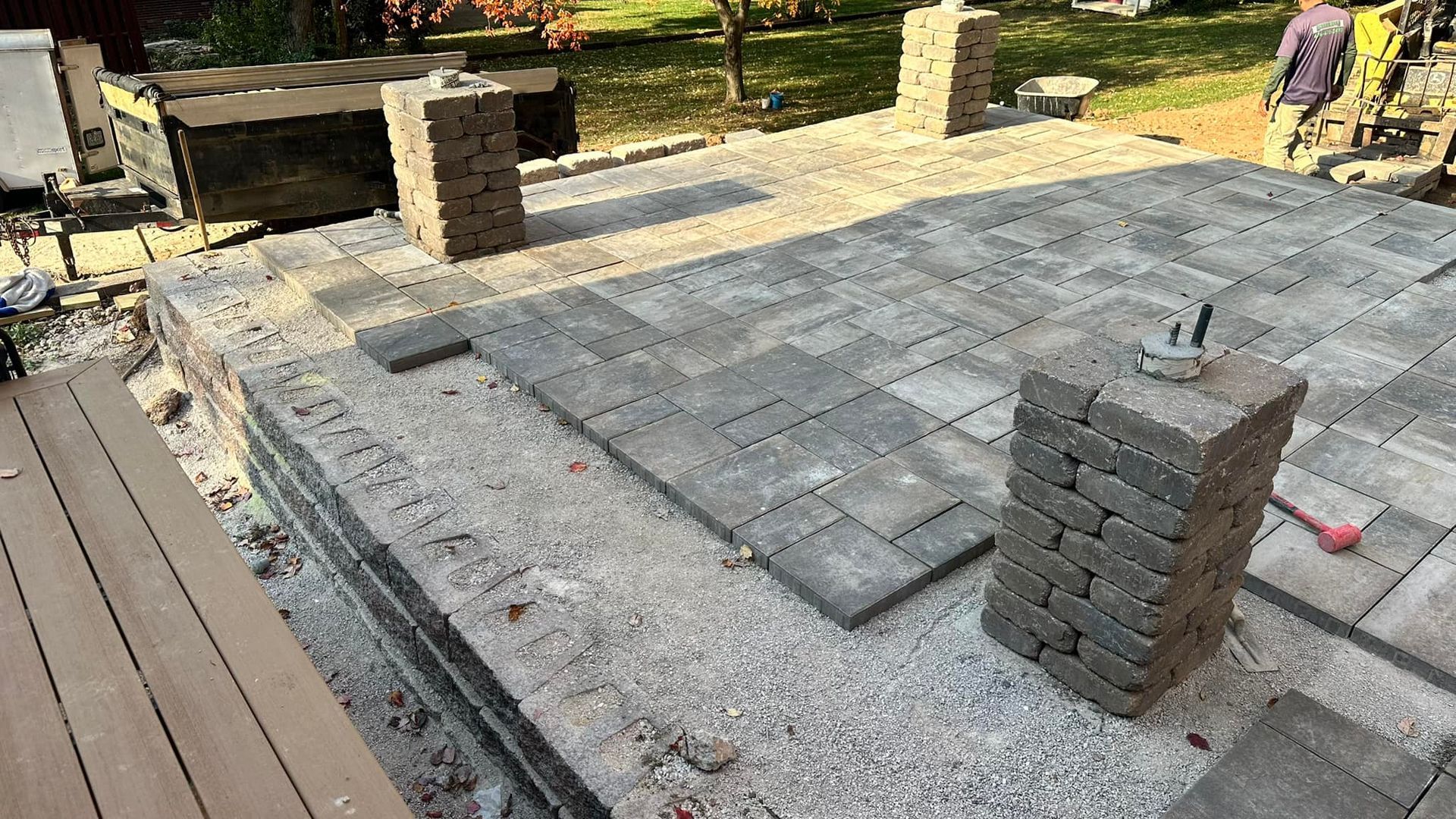 Construction of a patio with gray pavers; bricks stacked beside it.