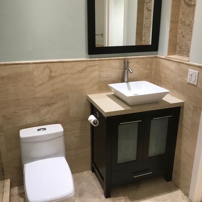 Small bathroom with toilet, vanity sink, and mirror against beige tile walls.