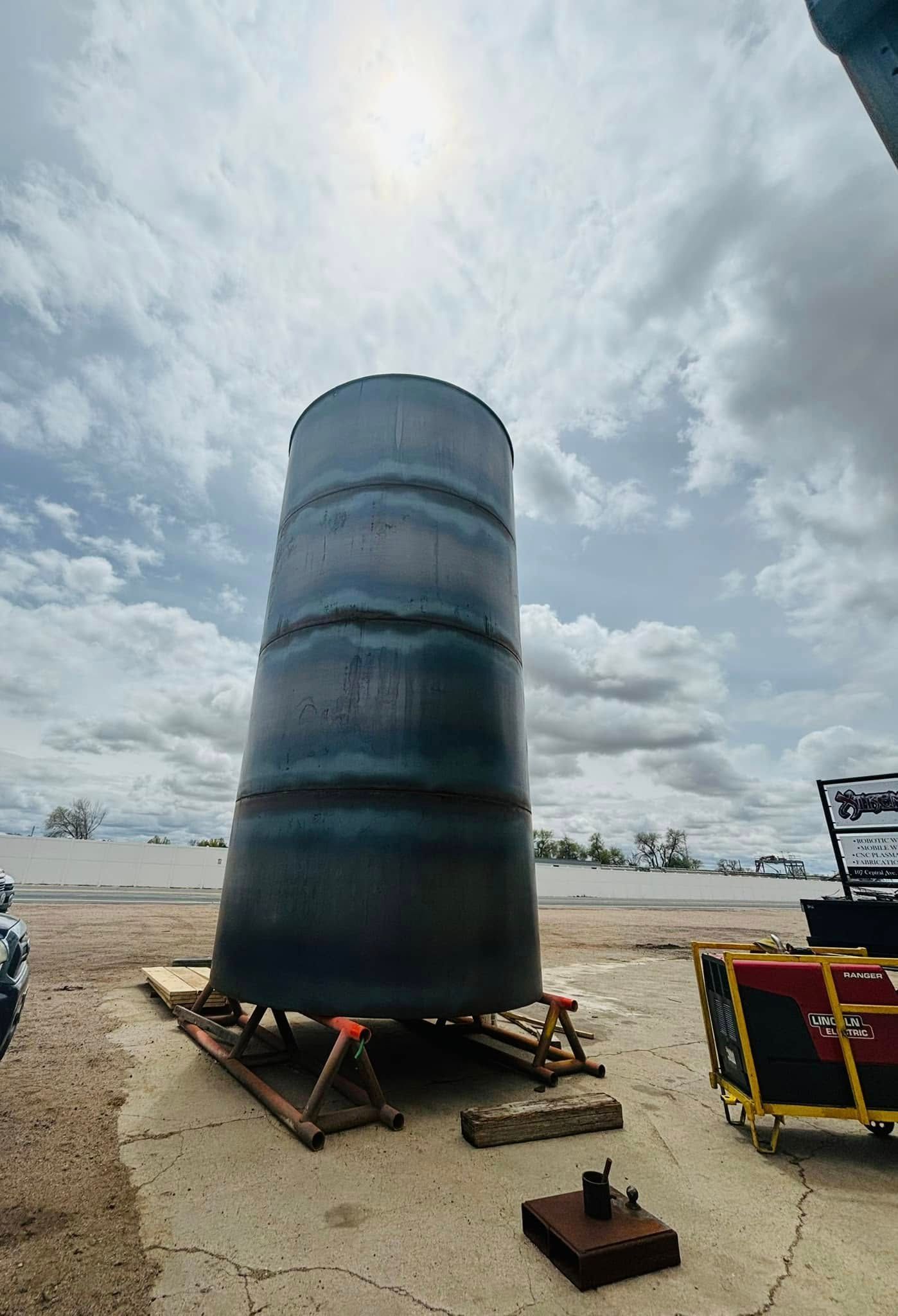 A large metal cylinder is sitting on the ground in a parking lot.