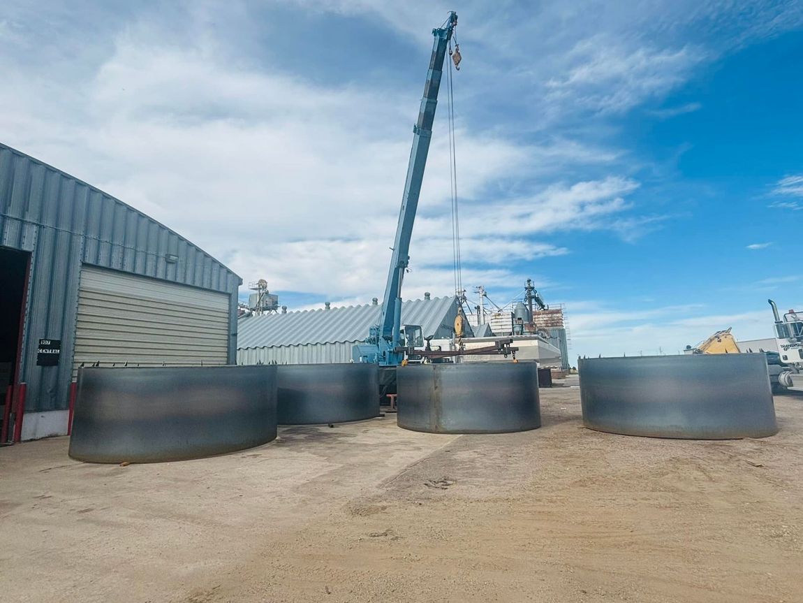 A crane is lifting a large metal cylinder in front of a building