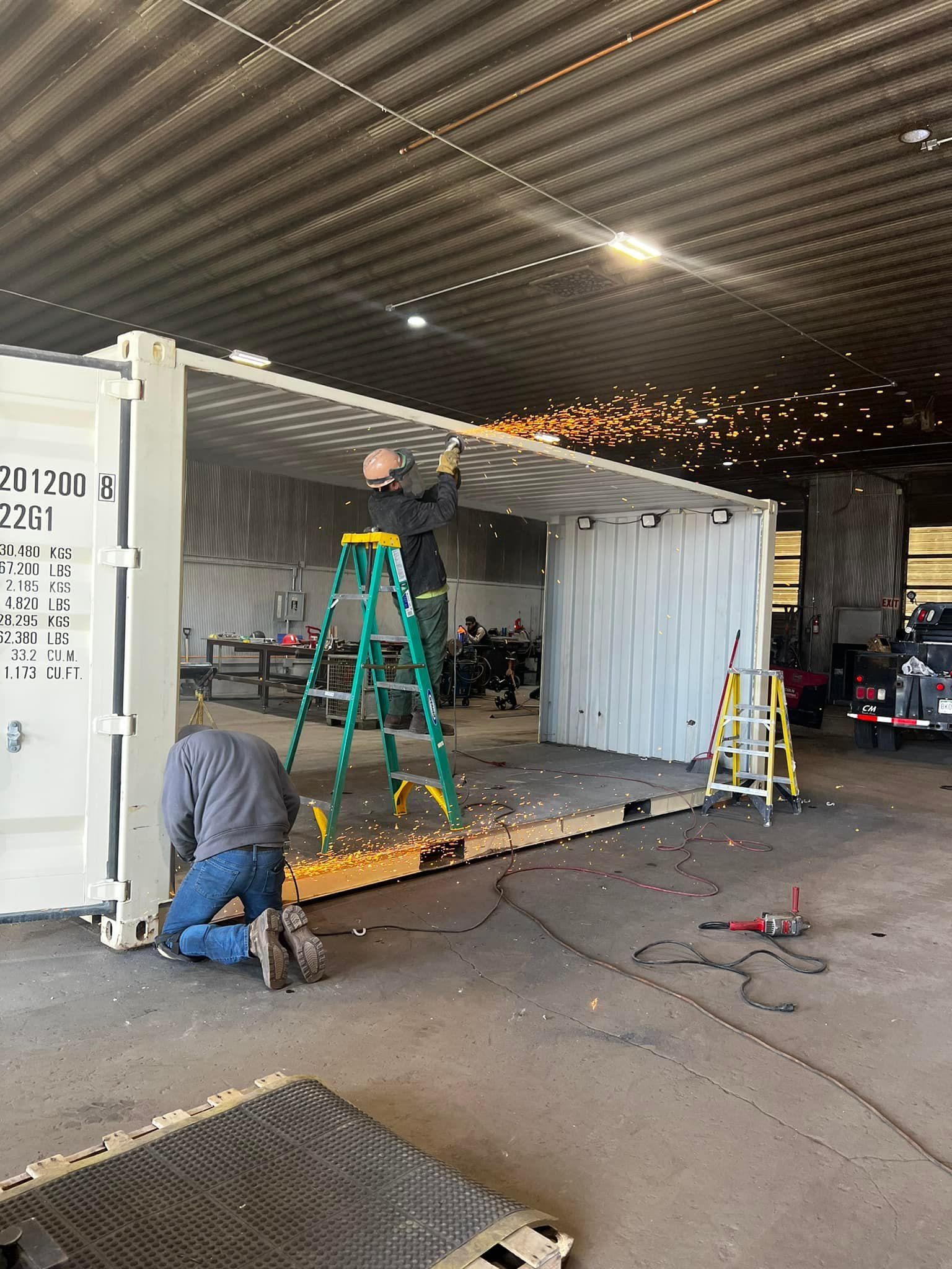 Two men are working on a shipping container in a garage.