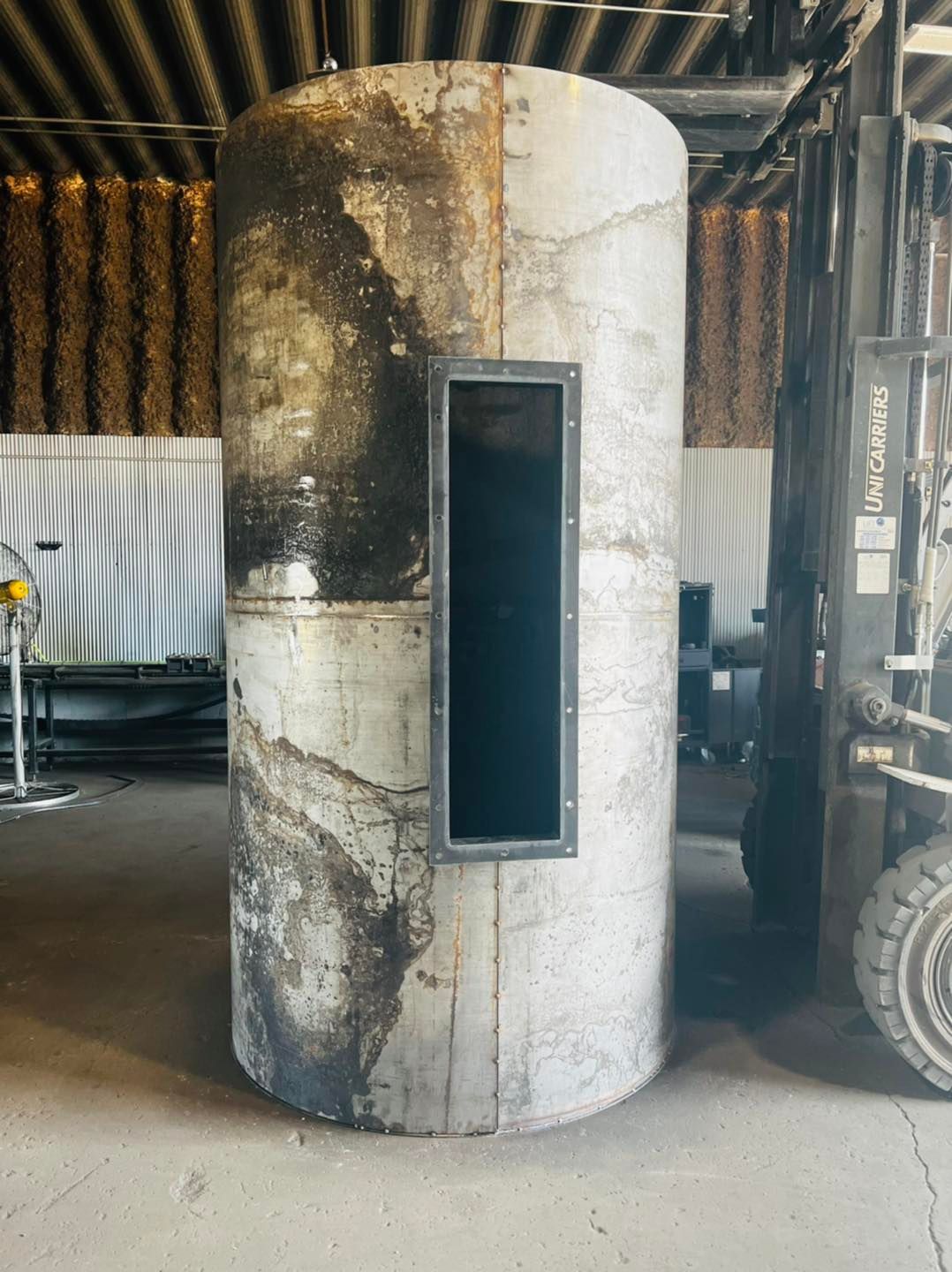 A large metal cylinder is sitting in a warehouse next to a forklift.