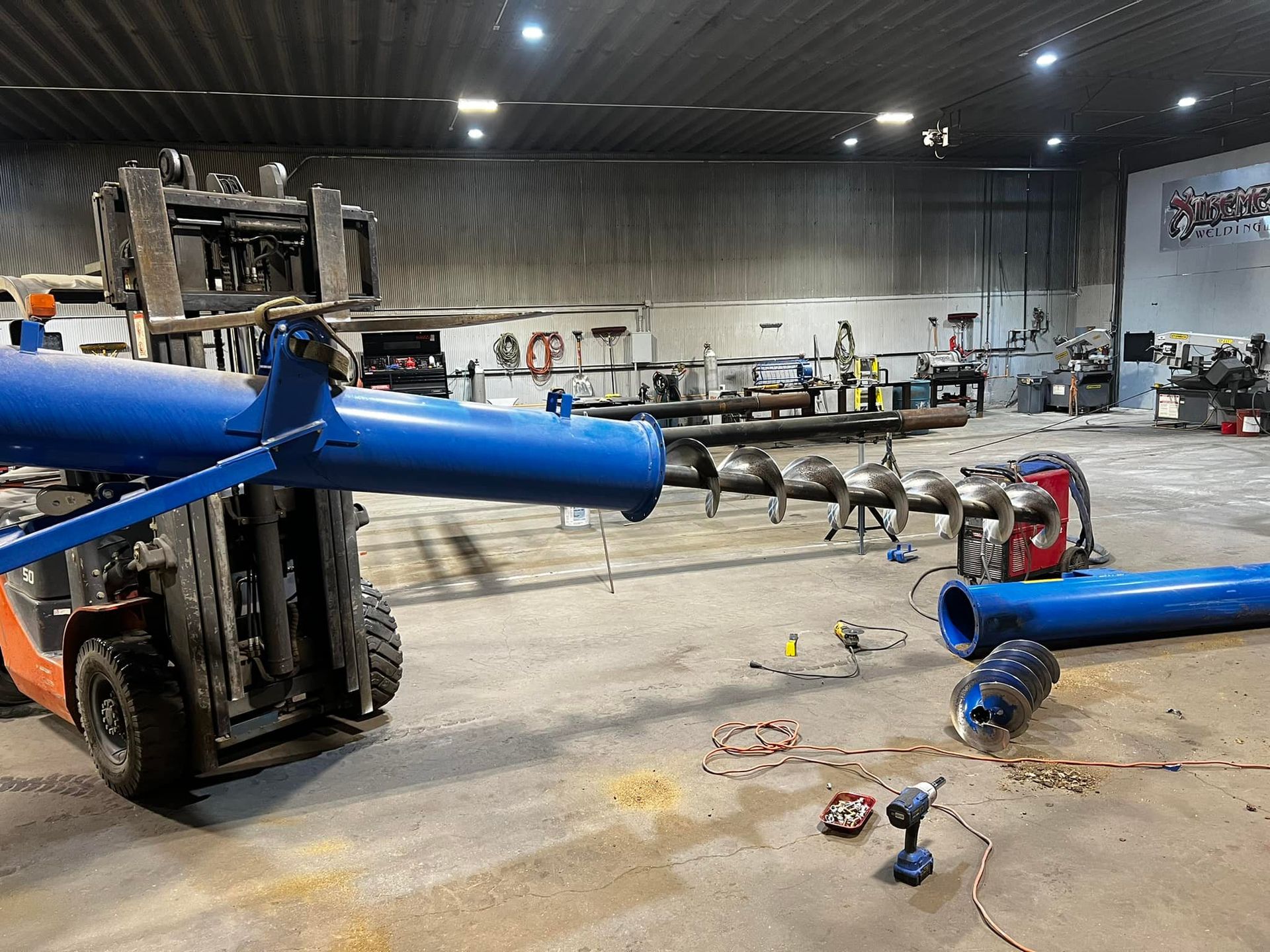 A forklift is carrying a blue pipe in a factory.