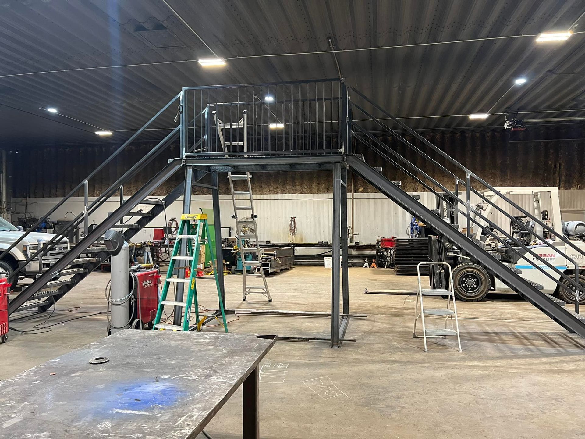 A metal staircase in a factory with a forklift in the background.