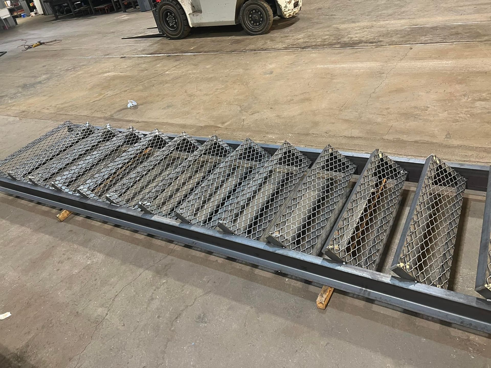 A metal ladder is sitting on the ground in a warehouse with a forklift in the background.