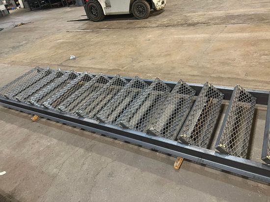 A metal ladder is sitting on the ground in a warehouse with a forklift in the background.