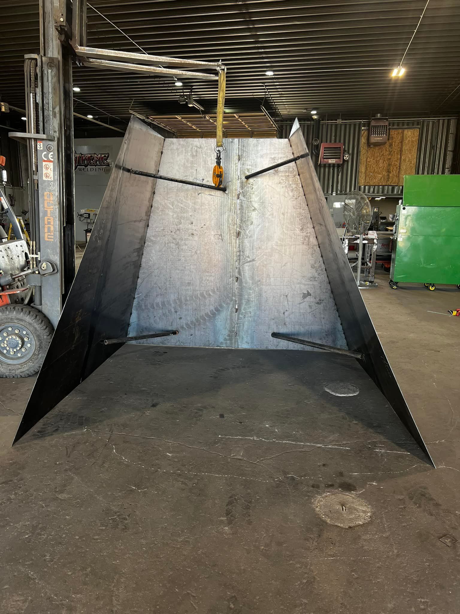 A large piece of metal is sitting in a warehouse next to a forklift.
