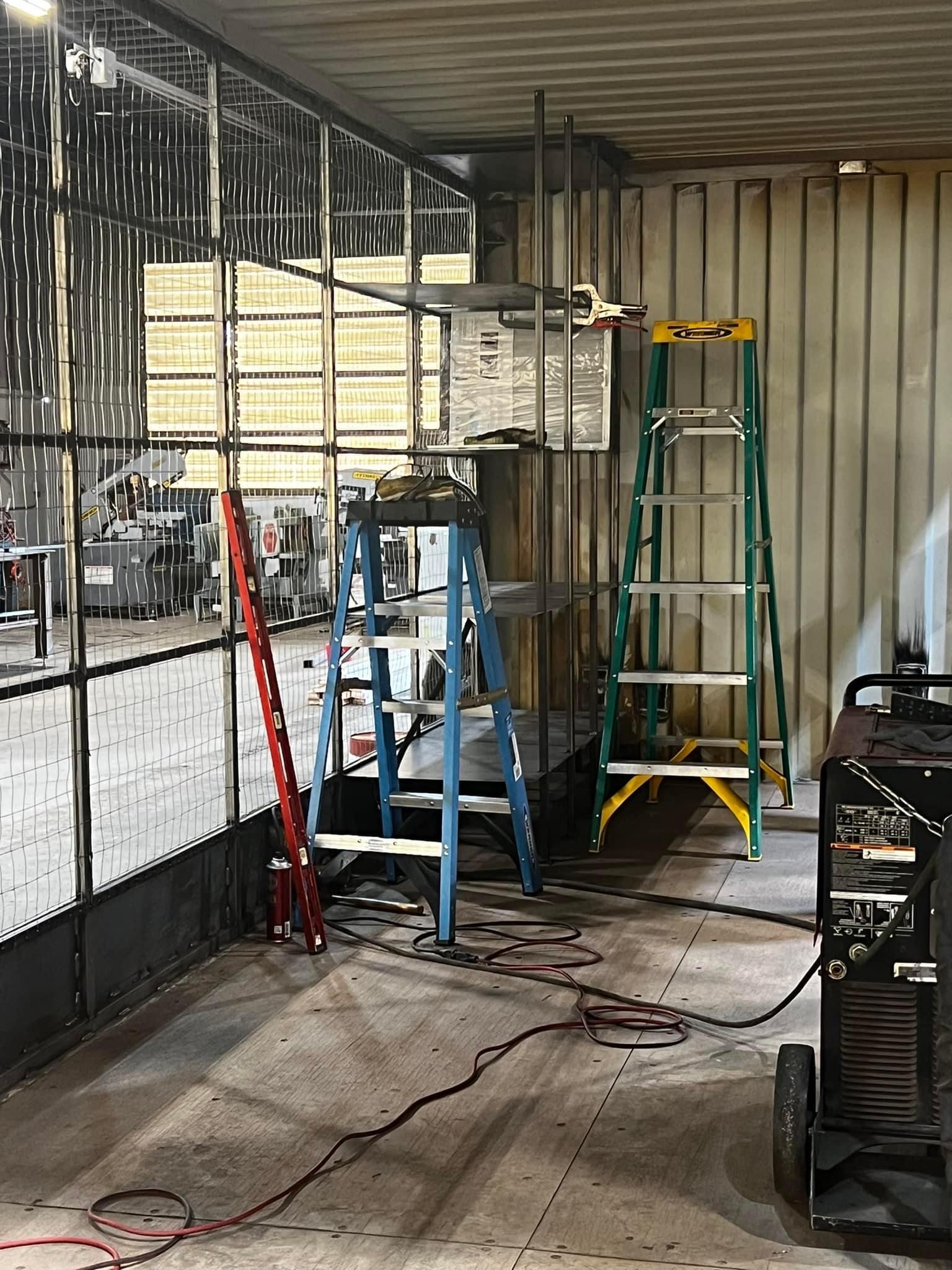 A room with a welding machine and ladder in it.