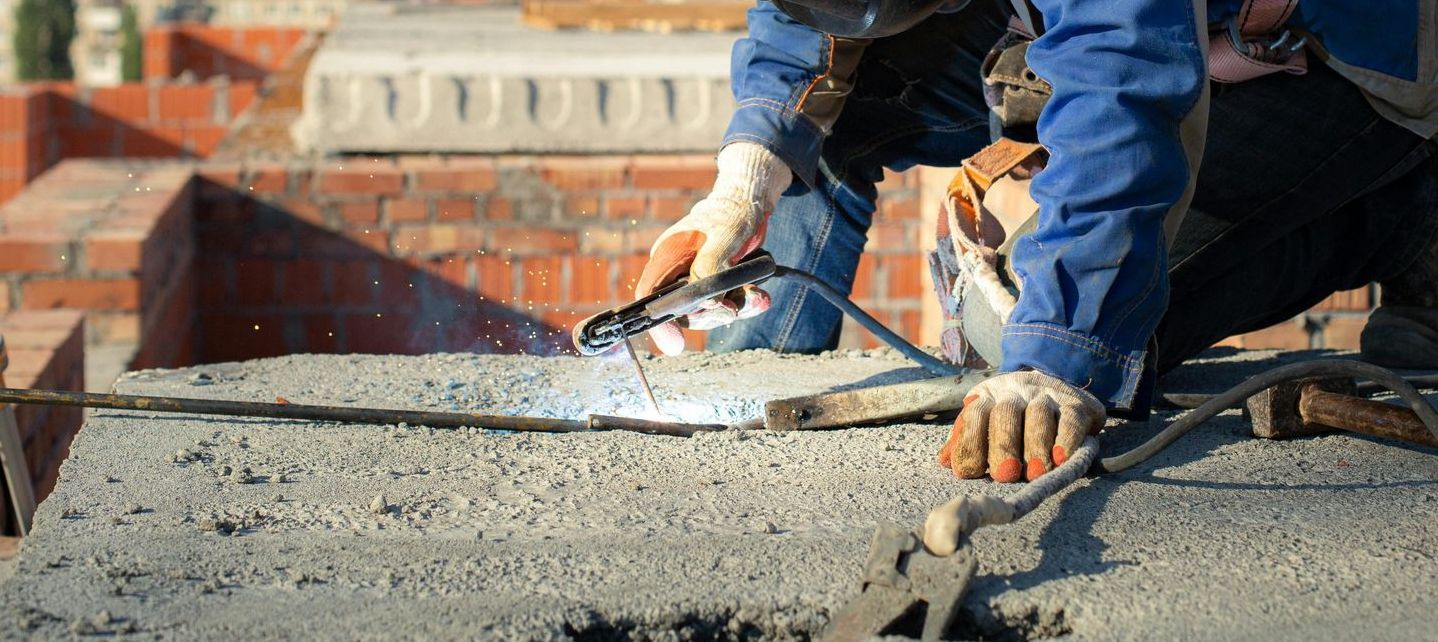 A man is welding a piece of metal on a brick wall.