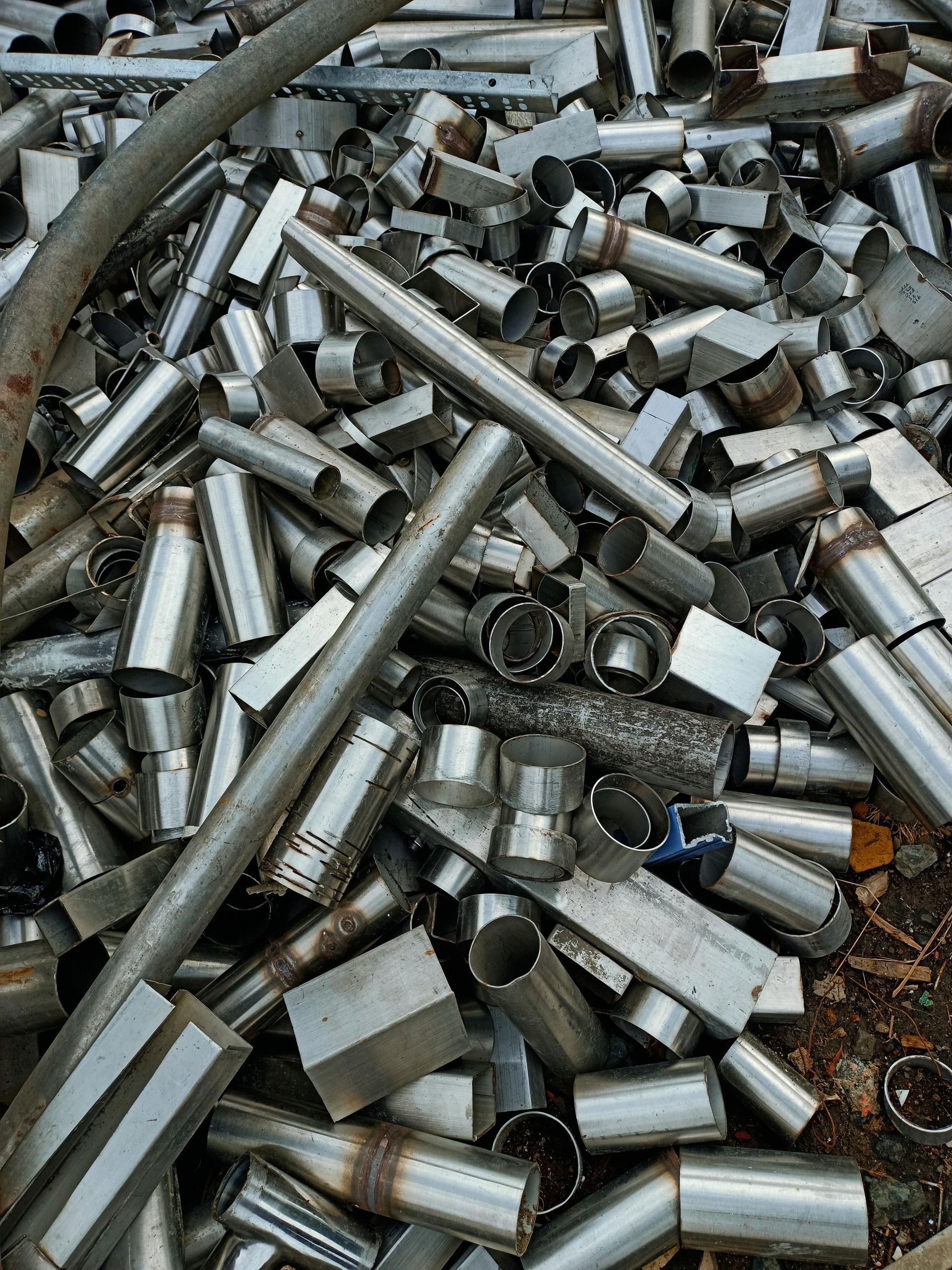 A pile of stainless steel pipes and tubes is sitting on the ground.