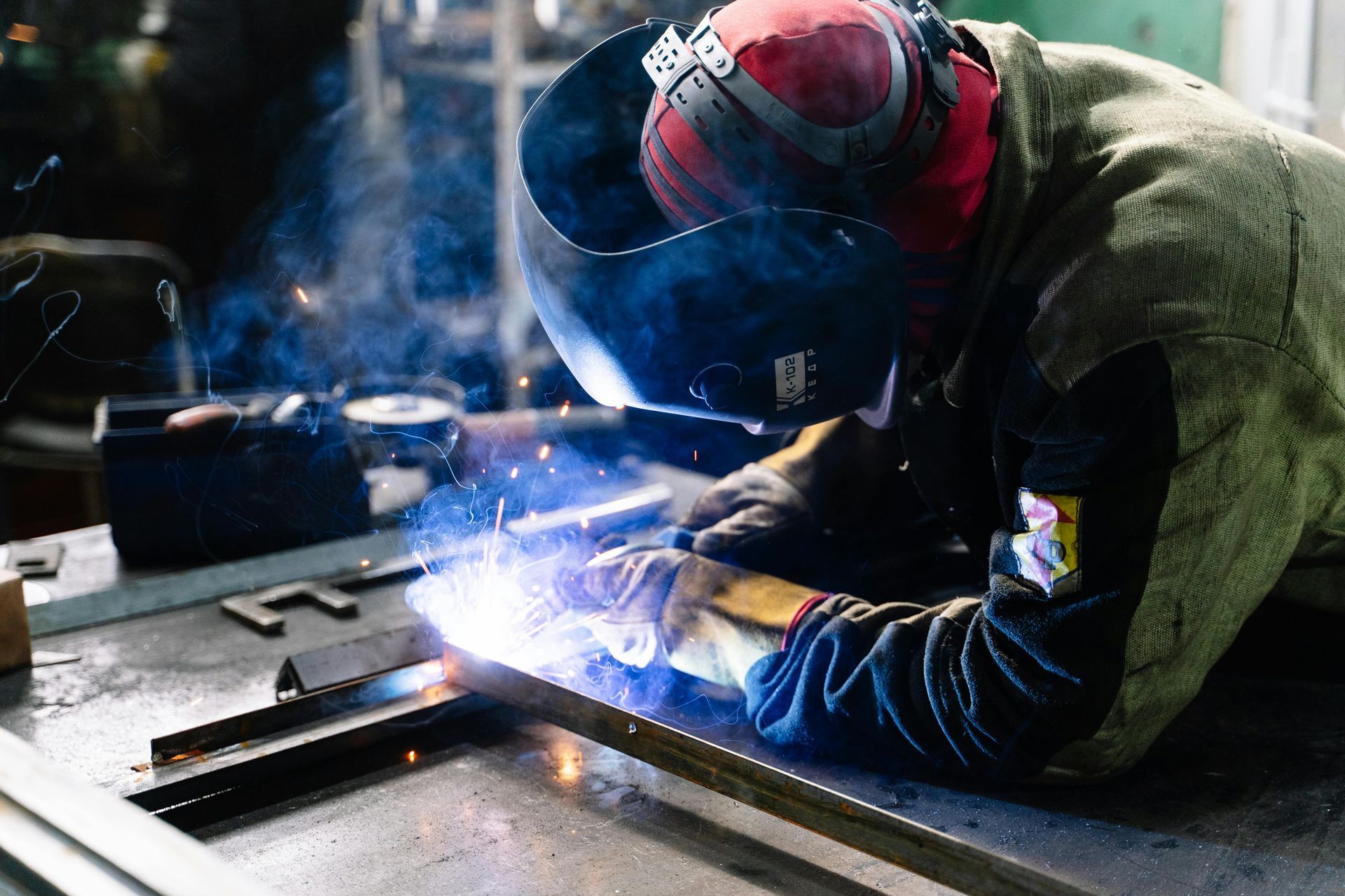 A man wearing a welding helmet is welding a piece of metal.