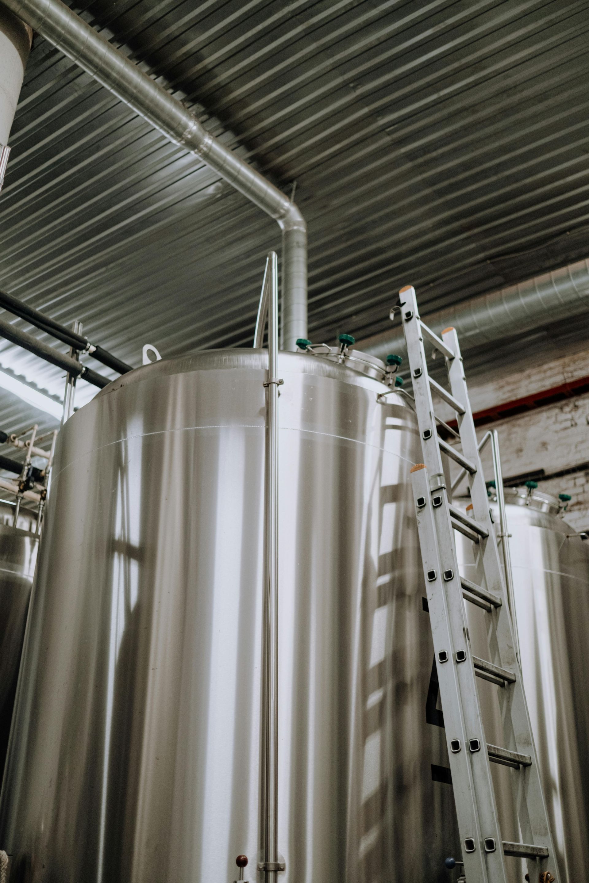 A ladder is sitting on top of a stainless steel tank in a factory.