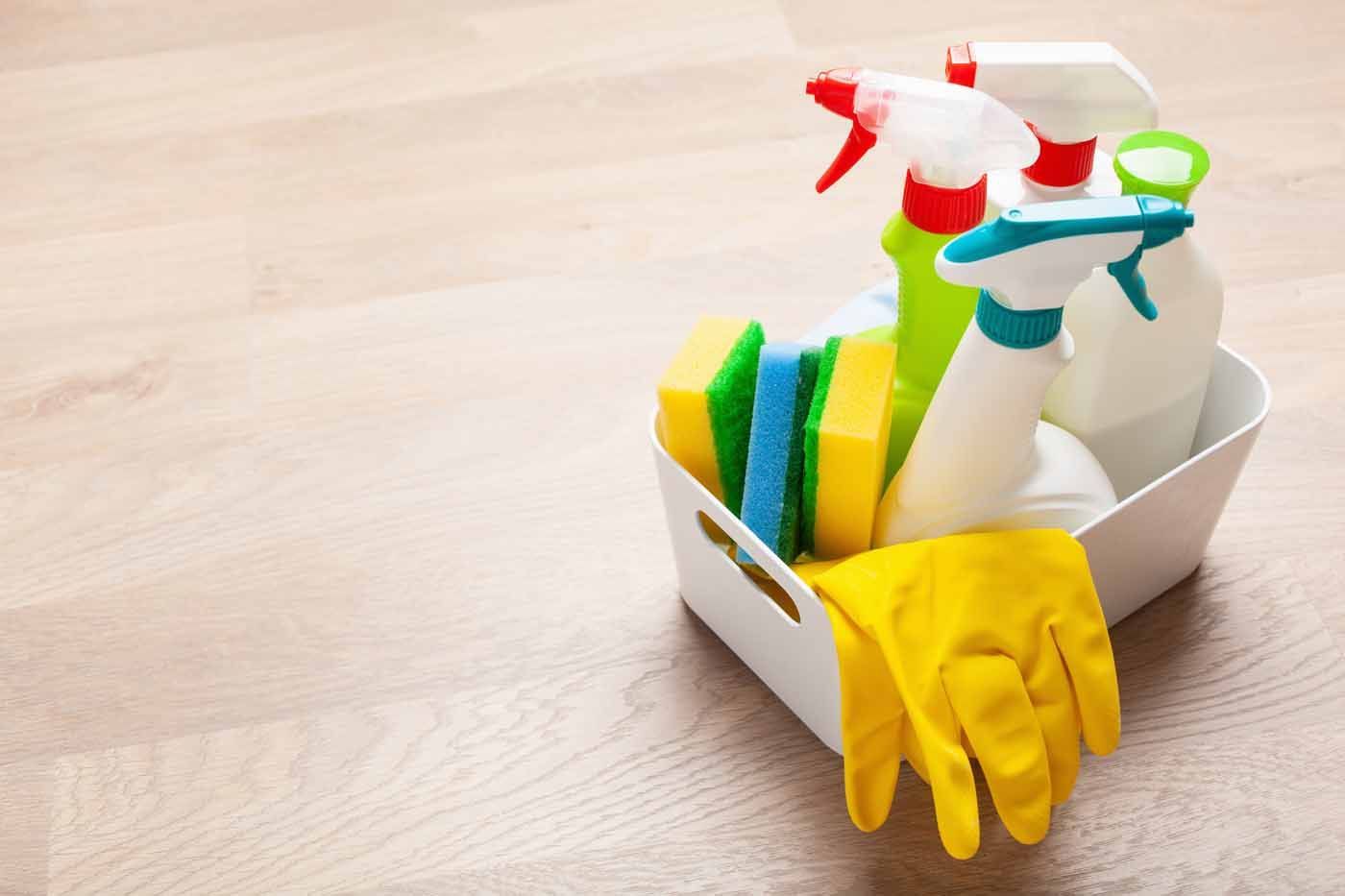 A basket filled with cleaning supplies and gloves on a wooden table.