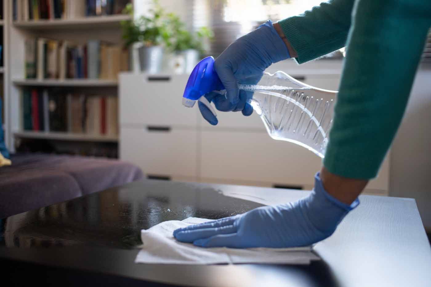 A person wearing blue gloves is cleaning a table with a spray bottle.