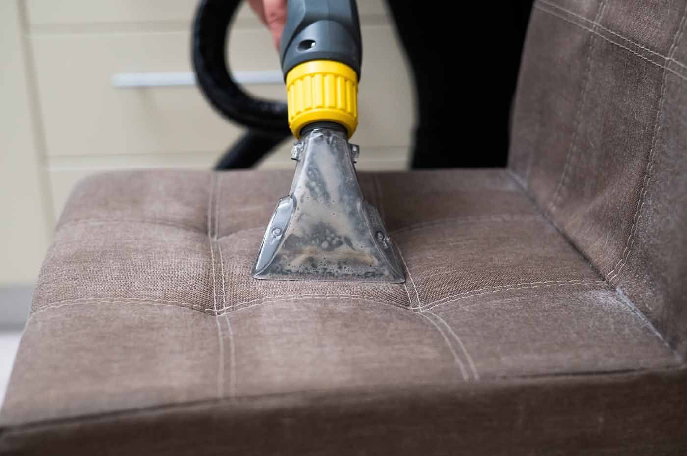 A person is cleaning a couch with a vacuum cleaner.