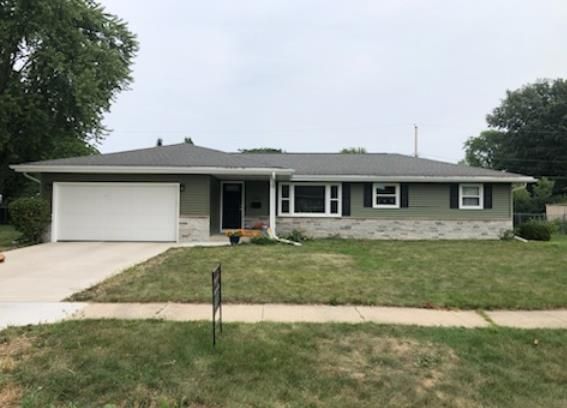 Ranch-style house with green siding, white garage door, and black-framed windows. Front lawn with sidewalk.