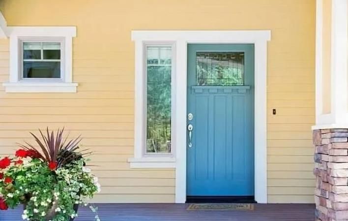 Blue front door with sidelight and window, set in a light yellow house with white trim.