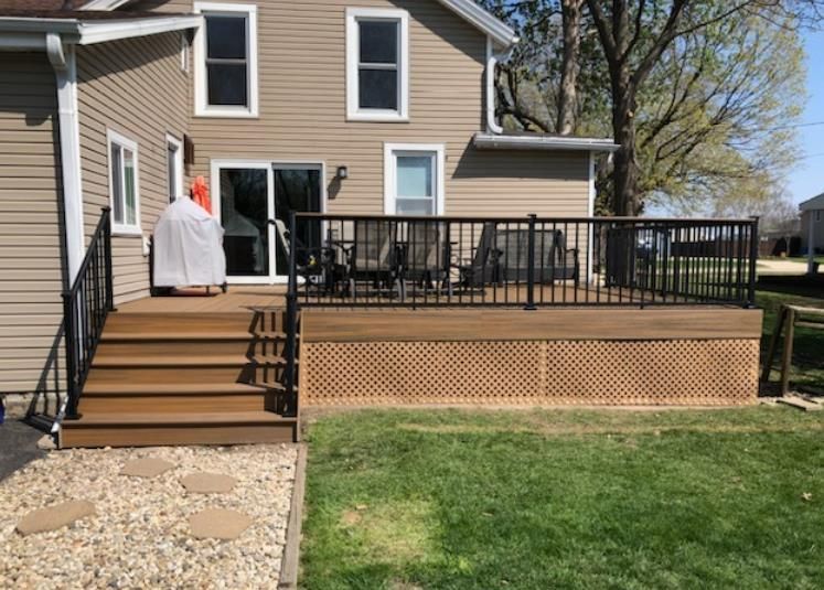 Backyard deck with brown composite deck boards, black railings, and lattice skirting against a beige house.